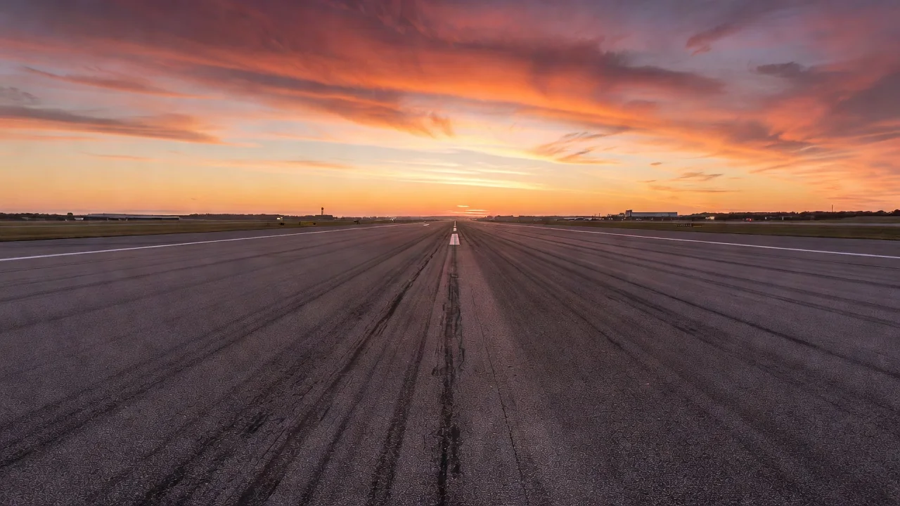 An airport runway stretching toward a colorful sunset sky